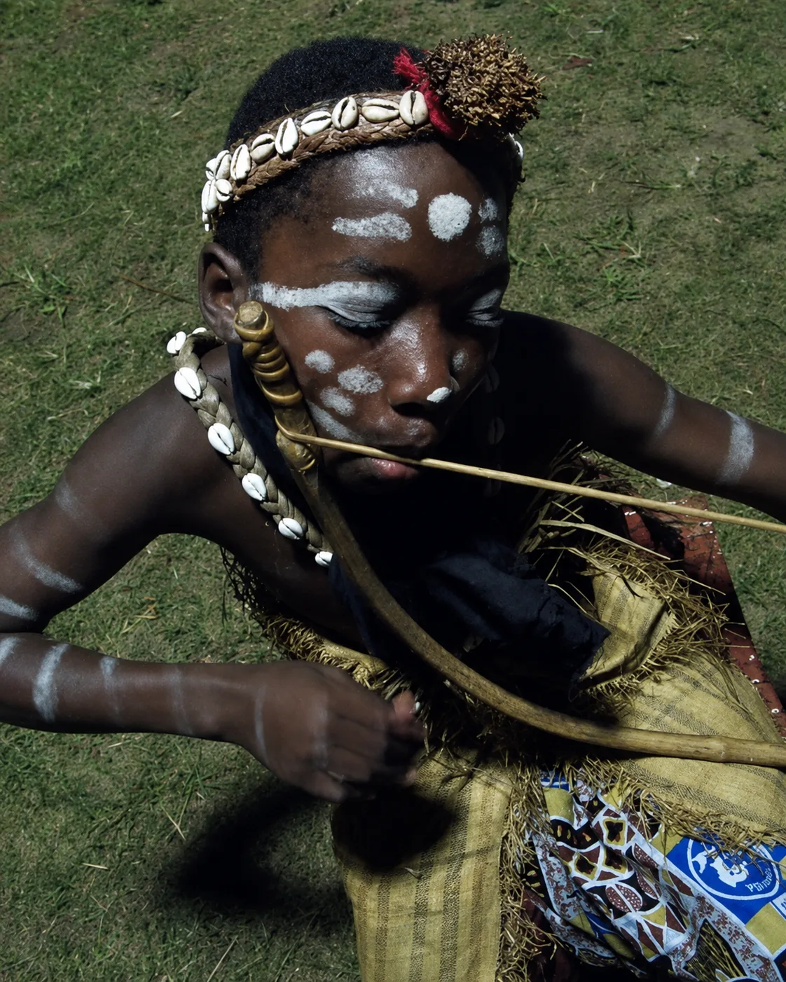 An initiate in quiet focus, body painted with kaolin, playing the musical bow before the ceremony