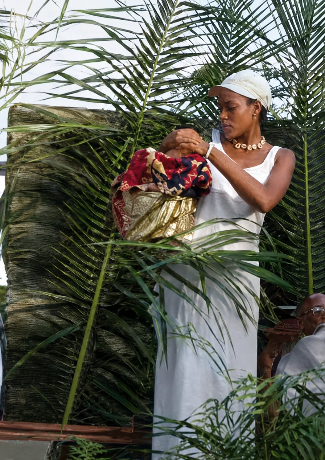 A woman receives a blessing during a ceremony, red raffia cloth — transmission within the community