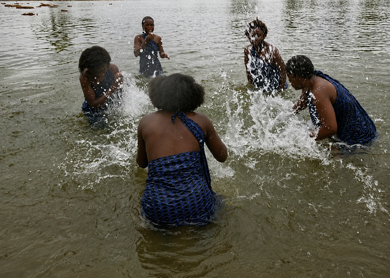 Young girls bathing in a river, splashing the clear water around them.