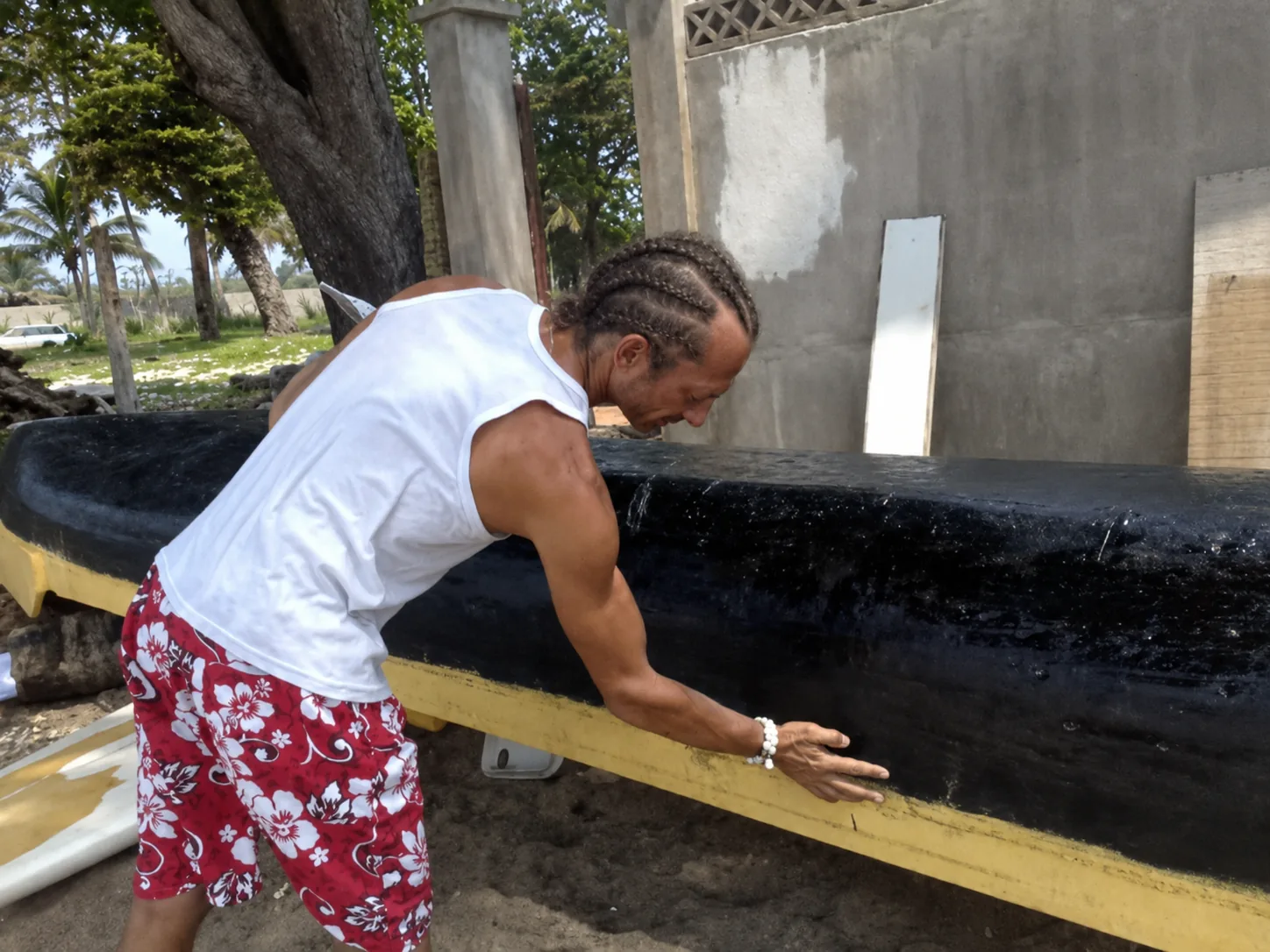 Pemba remet en état la pirogue, appuyé sur la coque réparée, sur la plage de La Sablière