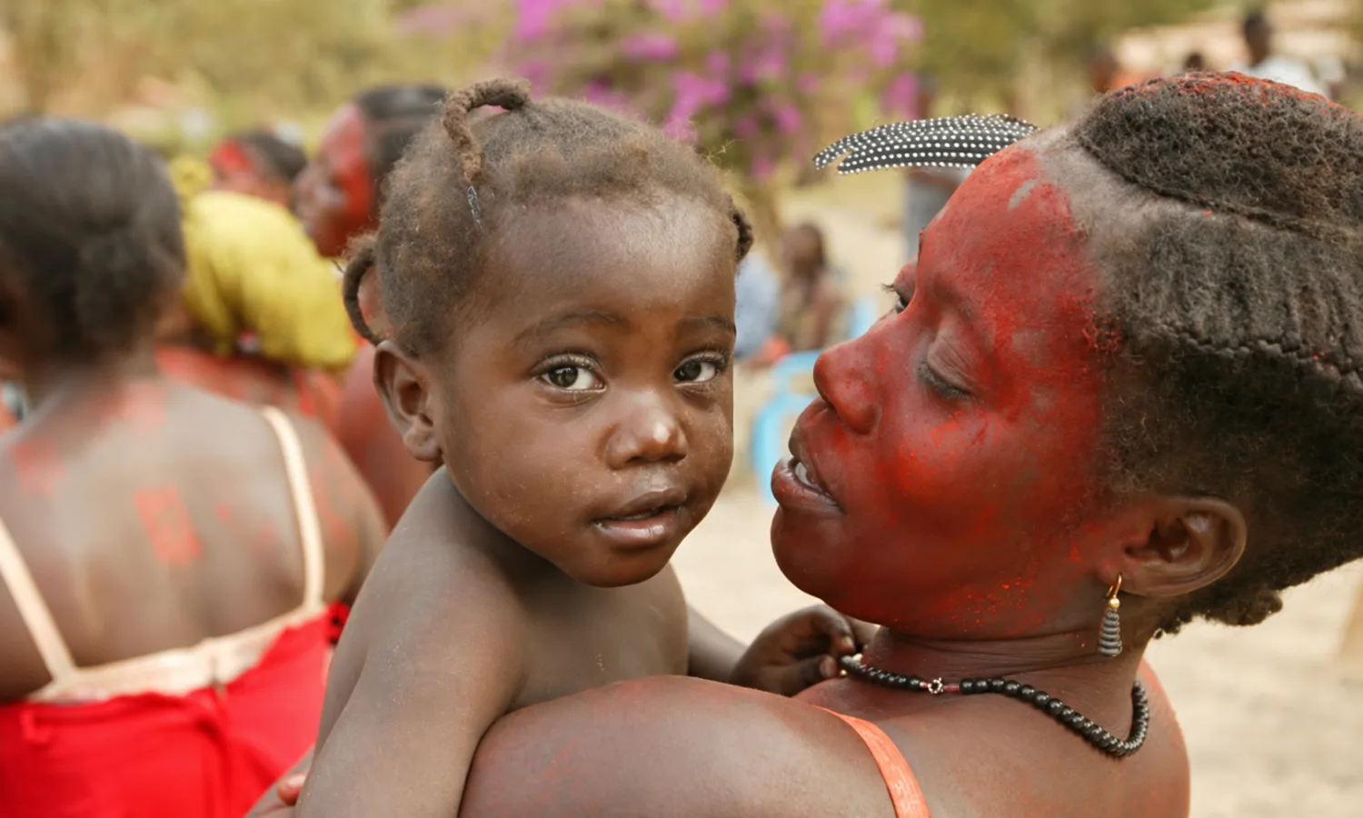 Une mère au visage peint de rouge tient sa fille dans ses bras lors d'un rassemblement villageois au Gabon
