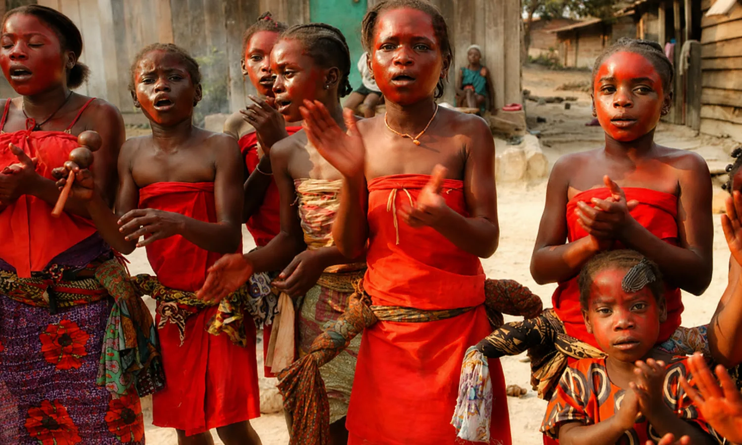 Des femmes chantent et agitent des hochets, vêtues de pagnes rouges